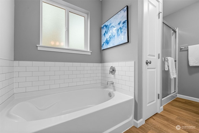 full bathroom with a stall shower, baseboards, a bath, and wood finished floors