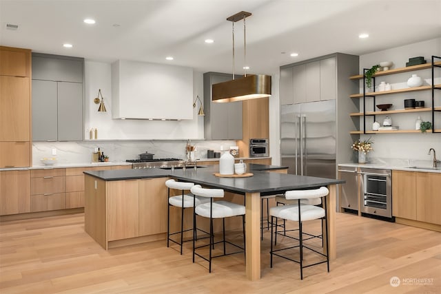 kitchen with a breakfast bar area, a center island with sink, beverage cooler, and light wood-type flooring