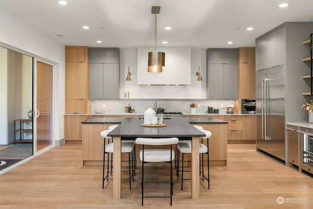 kitchen with light wood-type flooring, appliances with stainless steel finishes, decorative light fixtures, and a center island