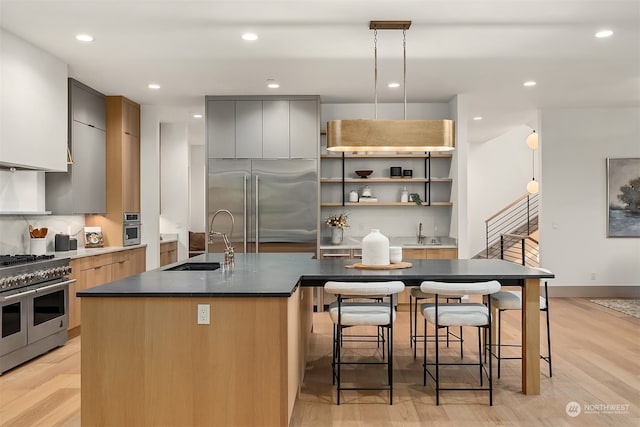 kitchen with premium appliances, light wood-type flooring, decorative light fixtures, and an island with sink