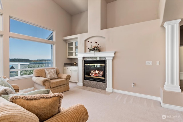 carpeted living room with a water view, decorative columns, a high end fireplace, and a towering ceiling