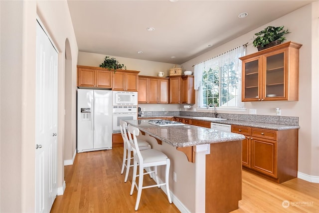 kitchen with light stone counters, white appliances, light hardwood / wood-style flooring, and a center island