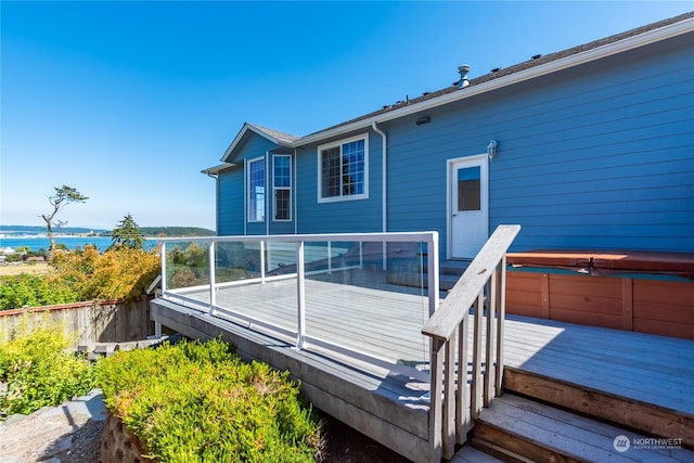 rear view of property with a deck with water view and a covered hot tub