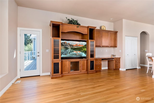 unfurnished living room featuring built in desk and light hardwood / wood-style floors