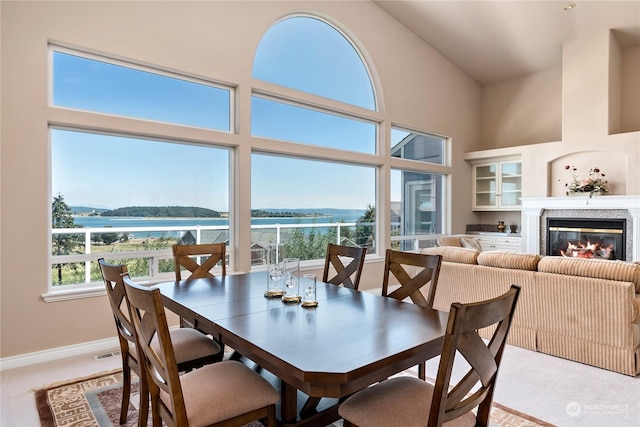 dining area featuring a high ceiling, a water view, and light colored carpet