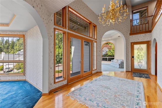 foyer entrance with wood-type flooring, a high ceiling, a raised ceiling, and a chandelier