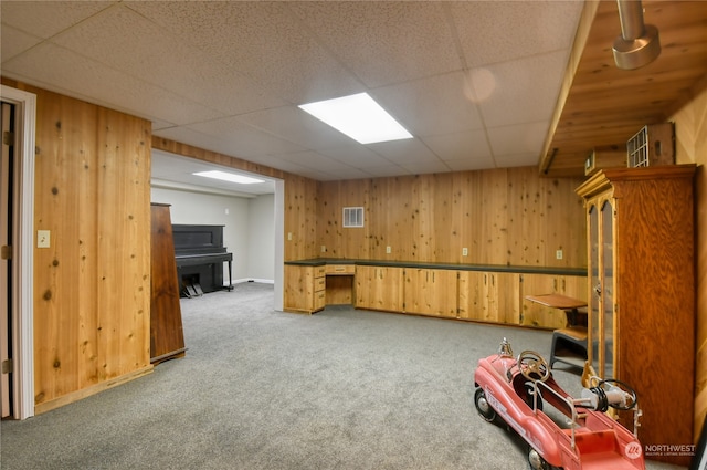 basement featuring wood walls, carpet floors, and a paneled ceiling