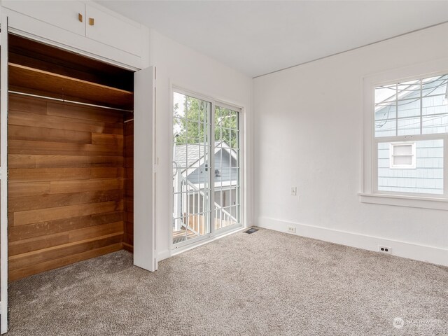 unfurnished bedroom featuring a closet, wooden walls, and carpet