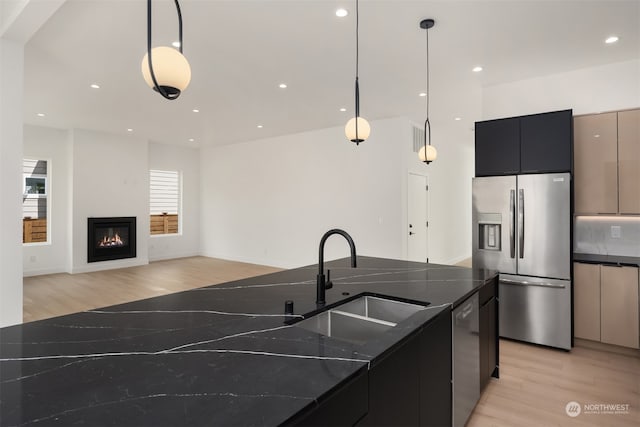 kitchen featuring stainless steel appliances, light hardwood / wood-style floors, decorative light fixtures, and a kitchen island with sink