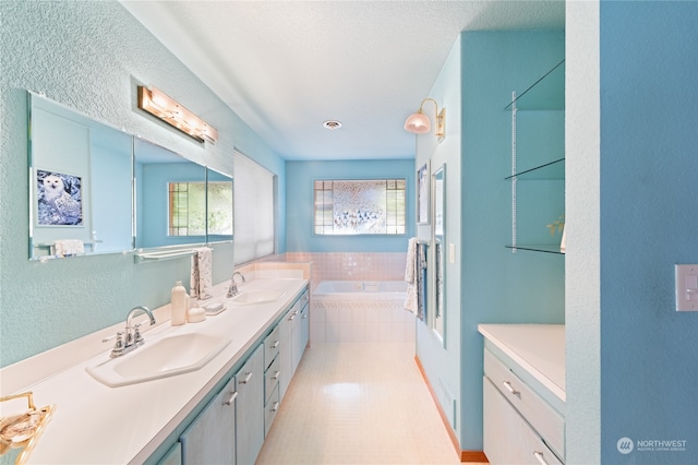 bathroom with a relaxing tiled tub, tile patterned floors, a textured ceiling, and vanity