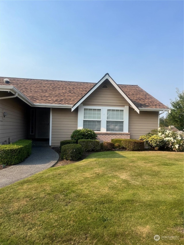 ranch-style house with brick siding, a front lawn, and roof with shingles