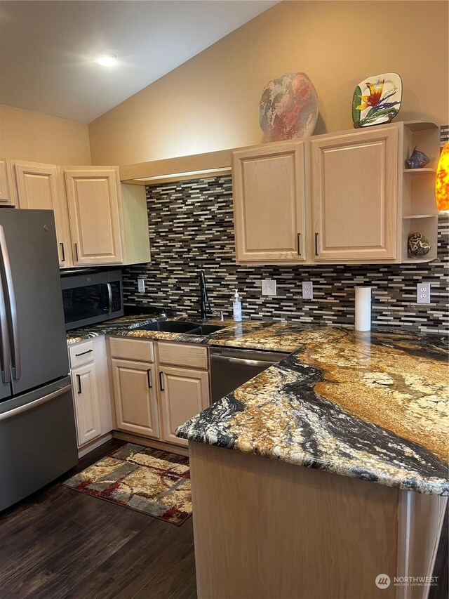 kitchen with dark stone countertops, appliances with stainless steel finishes, vaulted ceiling, backsplash, and sink