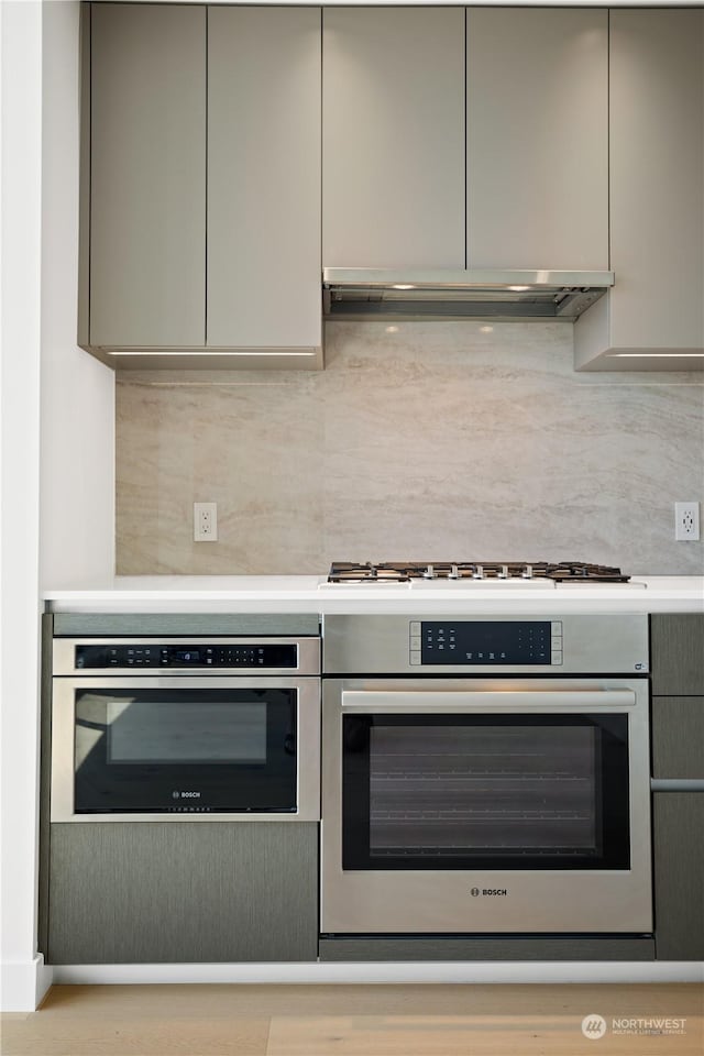 kitchen featuring tasteful backsplash, gray cabinets, range hood, and stainless steel oven