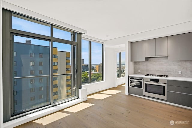 kitchen featuring backsplash, appliances with stainless steel finishes, light hardwood / wood-style floors, and gray cabinetry