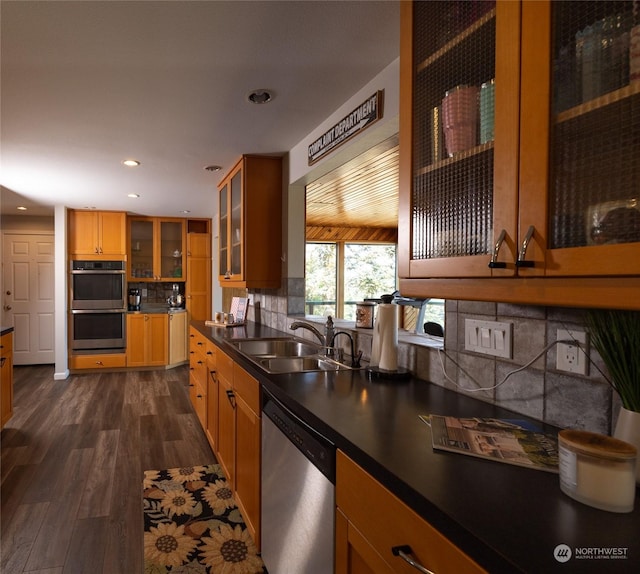 kitchen featuring dark wood-type flooring, a sink, dark countertops, appliances with stainless steel finishes, and glass insert cabinets