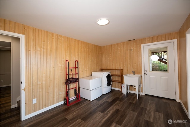 laundry room featuring wooden walls, washing machine and clothes dryer, dark wood finished floors, laundry area, and baseboards