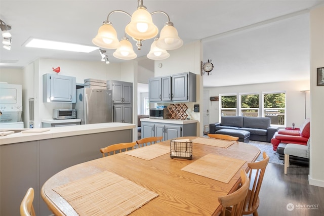 dining space featuring stacked washing maching and dryer, a chandelier, dark hardwood / wood-style flooring, and a skylight