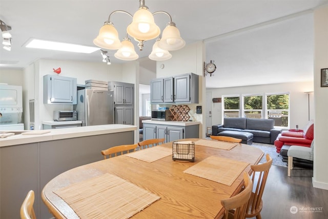 dining area featuring a notable chandelier, a toaster, dark wood finished floors, and stacked washer / drying machine