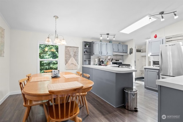 dining area featuring sink, an inviting chandelier, dark hardwood / wood-style flooring, rail lighting, and a skylight