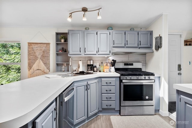 kitchen with appliances with stainless steel finishes, light countertops, under cabinet range hood, open shelves, and a sink