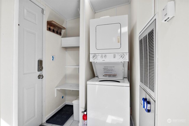 clothes washing area with light tile patterned flooring, stacked washer and dryer, and ornamental molding