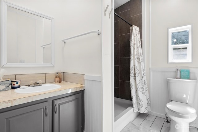 full bath with toilet, a stall shower, wainscoting, and vanity