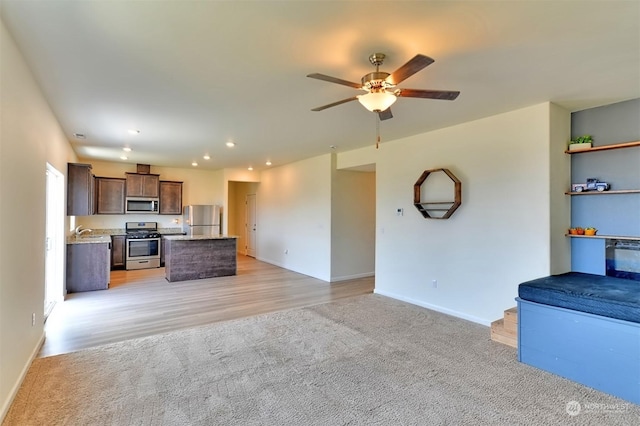 kitchen with sink, ceiling fan, stainless steel appliances, a kitchen island, and light colored carpet