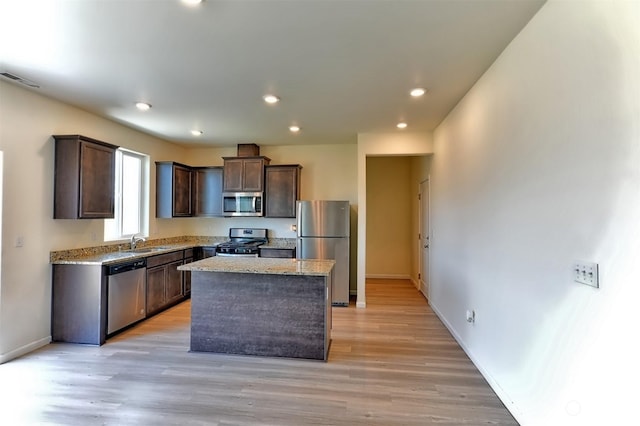 kitchen with sink, light stone counters, a center island, dark brown cabinets, and appliances with stainless steel finishes