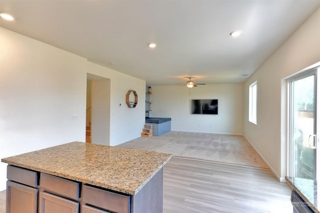 kitchen with light stone counters, ceiling fan, and light wood-type flooring