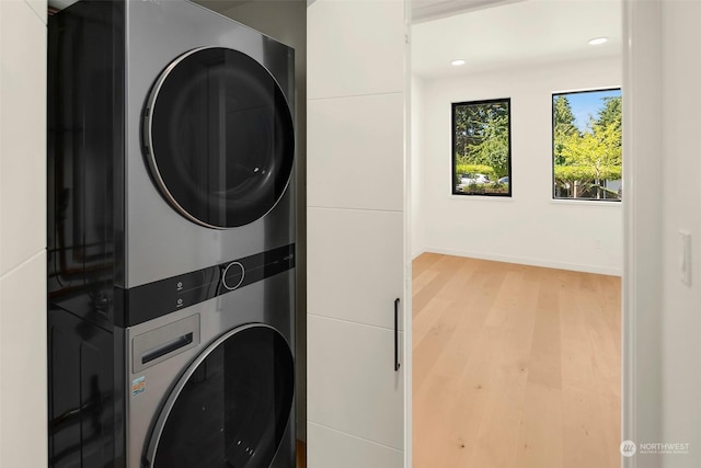 washroom with light hardwood / wood-style floors and stacked washing maching and dryer