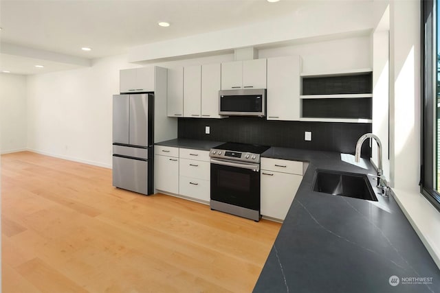 kitchen with sink, light hardwood / wood-style flooring, appliances with stainless steel finishes, white cabinetry, and tasteful backsplash