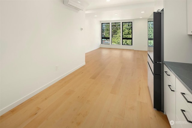 kitchen with a wall unit AC, light hardwood / wood-style floors, white cabinets, and refrigerator