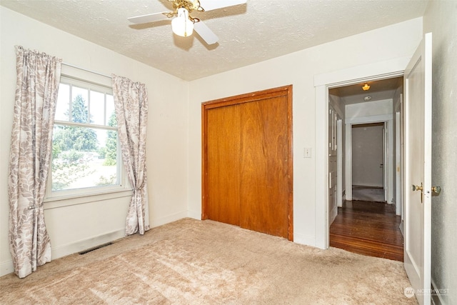 unfurnished bedroom with light carpet, ceiling fan, a closet, and a textured ceiling