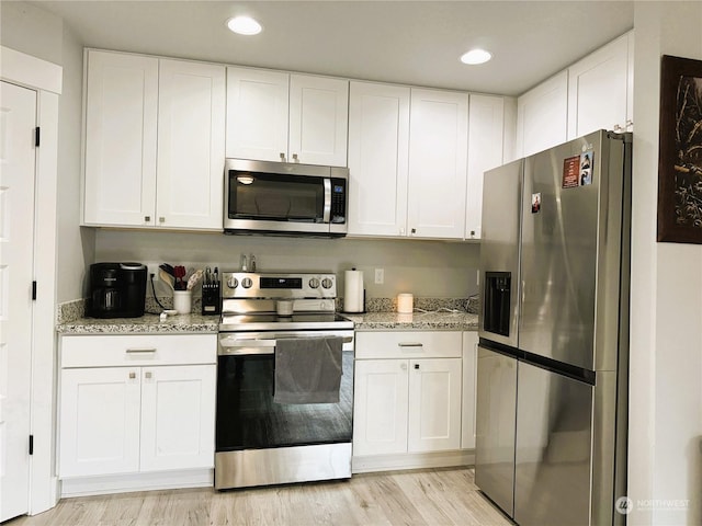 kitchen featuring appliances with stainless steel finishes, light stone countertops, light wood-type flooring, and white cabinets