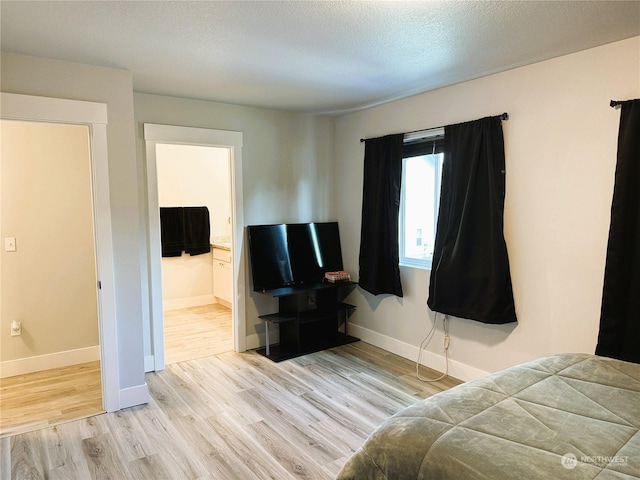 bedroom with ensuite bathroom, light hardwood / wood-style flooring, and a textured ceiling