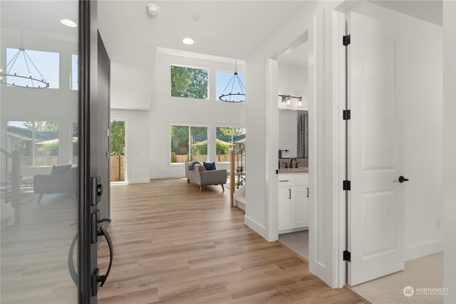 hall with a towering ceiling, sink, light hardwood / wood-style floors, and a notable chandelier