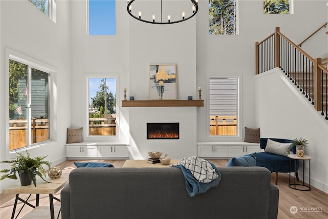 living room featuring a towering ceiling, a fireplace, a chandelier, and light hardwood / wood-style floors