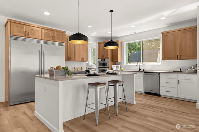 kitchen with appliances with stainless steel finishes, a kitchen island, white cabinetry, hanging light fixtures, and light hardwood / wood-style flooring