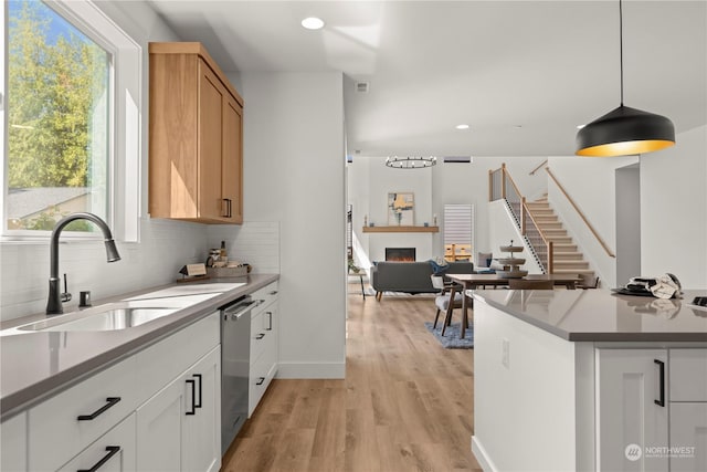 kitchen featuring white cabinetry, stainless steel dishwasher, sink, and hanging light fixtures