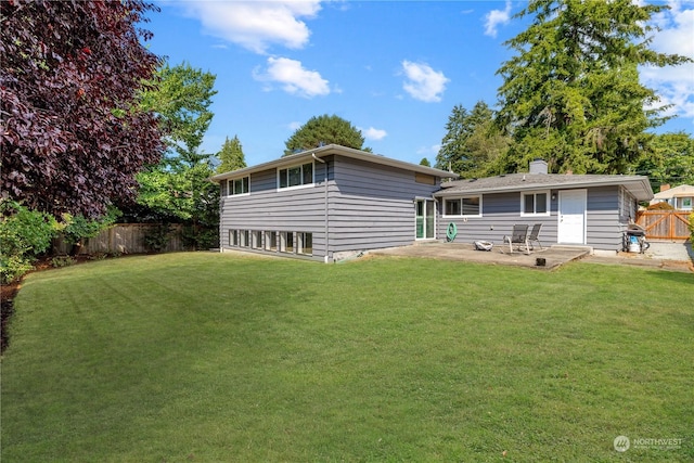 rear view of house with a patio, a lawn, a chimney, and a fenced backyard