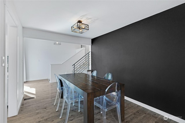 dining space featuring baseboards, visible vents, stairway, wood finished floors, and a notable chandelier