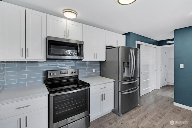 kitchen featuring tasteful backsplash, white cabinets, stainless steel appliances, light countertops, and light wood-type flooring