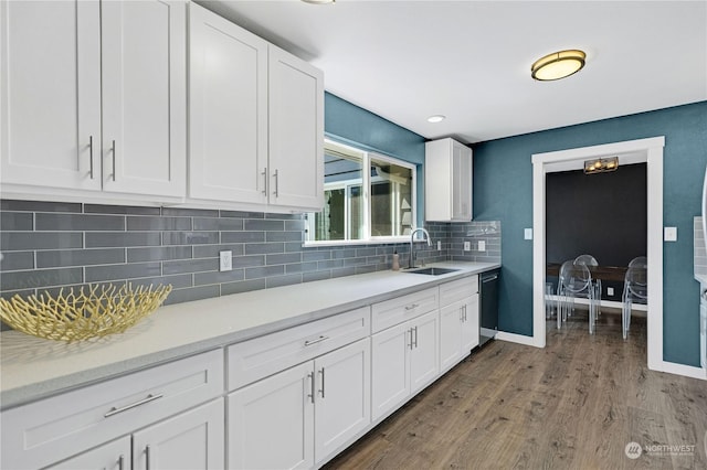 kitchen with light countertops, white cabinetry, a sink, wood finished floors, and dishwashing machine