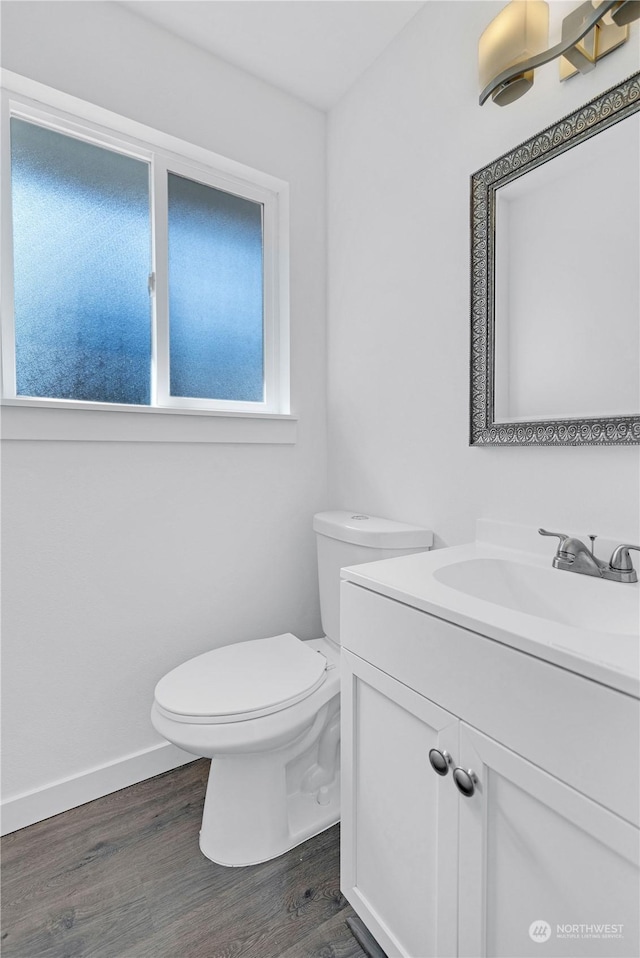 half bath with baseboards, vanity, toilet, and wood finished floors