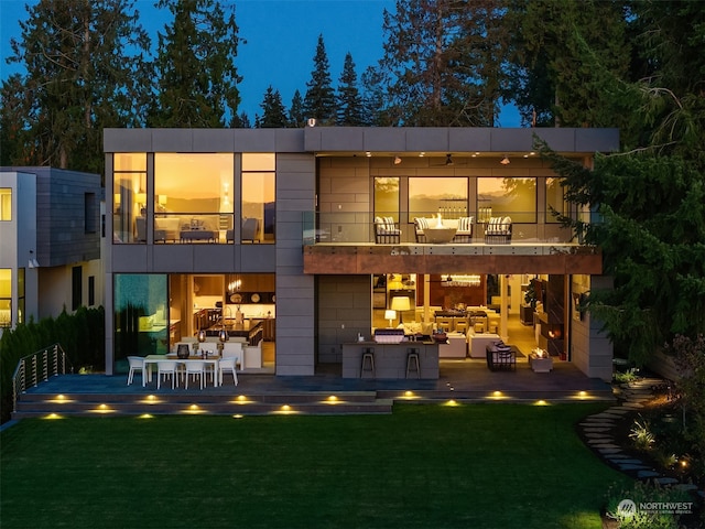 back house at twilight with a balcony, a yard, and a patio