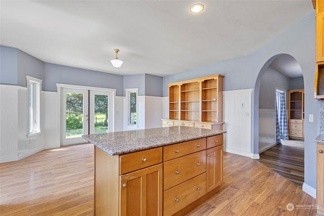 kitchen with french doors, light stone countertops, light wood-type flooring, and a kitchen island