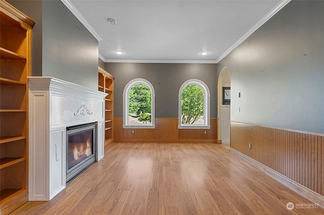 unfurnished living room featuring ornamental molding, wooden walls, and light wood-type flooring