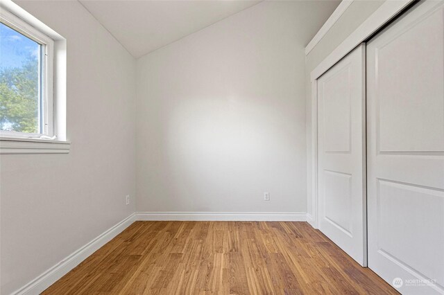 unfurnished bedroom featuring vaulted ceiling, a closet, and light wood-type flooring