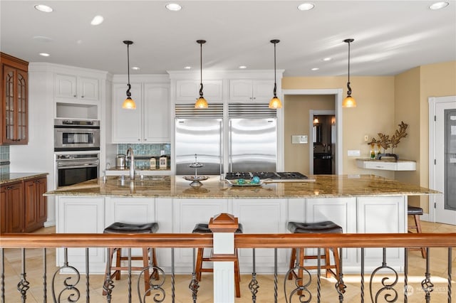 kitchen with sink, appliances with stainless steel finishes, white cabinetry, a center island with sink, and decorative light fixtures