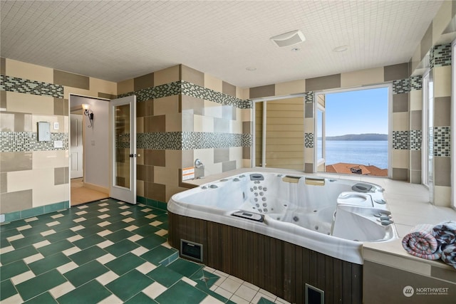 bathroom featuring a water view, a bathing tub, and tile walls